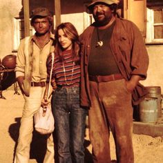 two men and a woman standing in front of a building with an old fashion hat on