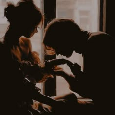 a man and woman sitting next to each other in front of a window looking at their cell phones