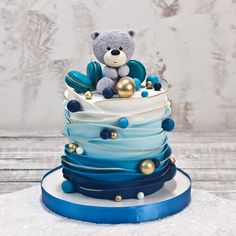 a teddy bear sitting on top of a multi layer cake with blue and gold decorations