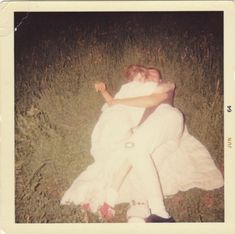 a woman in white dress sitting on the ground with her arms around another woman's neck