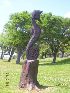 a sculpture in the shape of a snake on top of a tree stump with grass and trees behind it