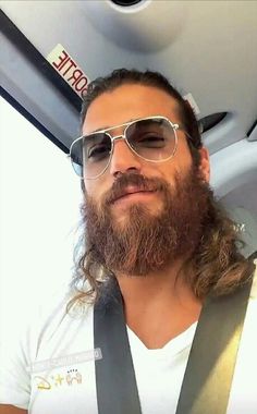 a man with long hair wearing sunglasses and suspenders in the back seat of a car