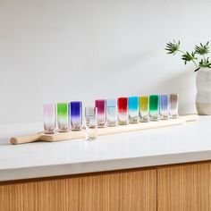 a row of colorful shot glasses sitting on top of a counter next to a vase