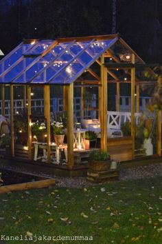 a small wooden structure with lights on it in the night time, surrounded by greenery and potted plants