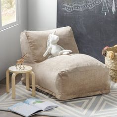 a stuffed animal sitting on top of a chair next to a basket and book in front of a chalkboard