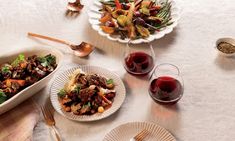 a table topped with plates of food next to glasses of wine and utensils