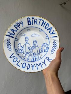 a hand holding a blue and white plate with the words happy birthday written on it