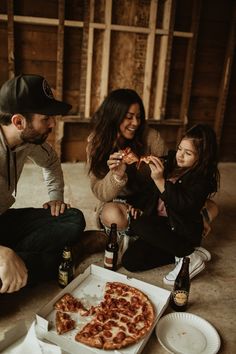 three people sitting on the floor eating pizza and drinking beer while one woman sits next to them