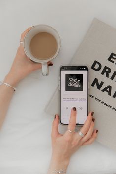 a woman using her cell phone while sitting at a table with a book and cup of coffee