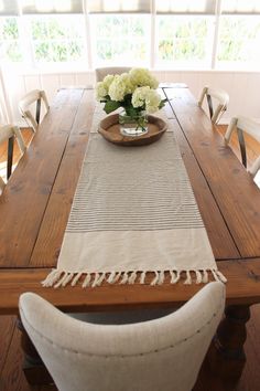 a wooden table with white chairs and flowers in a bowl on top of the table