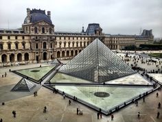 people are walking around in front of the glass pyramid