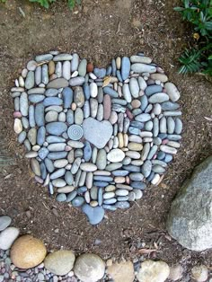 a heart made out of rocks sitting on top of a dirt ground next to some plants