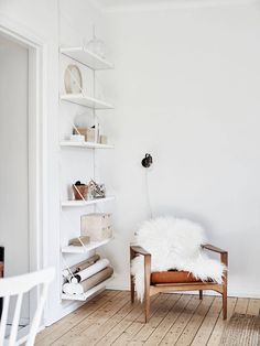 a white room with a chair and shelves on the wall, bookshelf in the corner