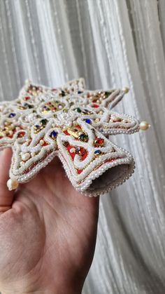 a hand holding a small white beaded star ornament