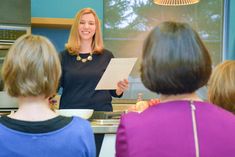 a woman standing in front of a group of people while holding papers and looking at the camera