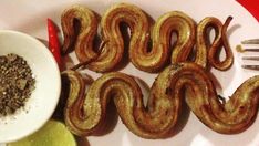 a white plate topped with fried snakes next to a fork and bowl filled with seasoning