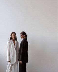 two women standing next to each other in front of a white wall, both wearing black and white clothing