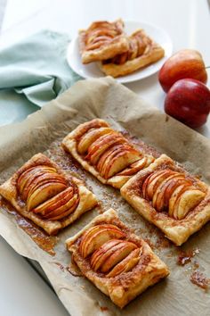 four pieces of apple tarts sitting on top of a piece of parchment paper next to some apples