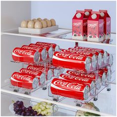 there are many cans of coca - cola on the shelves next to some fruit and eggs