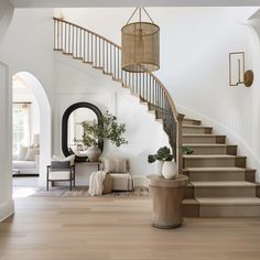 a staircase in a home with white walls and wood flooring is flanked by a round mirror