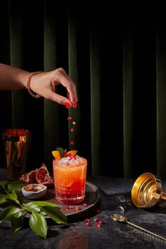 a woman is sprinkling red liquid on a cocktail