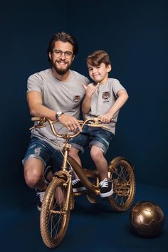 a man sitting on top of a bike next to a little boy in front of a soccer ball