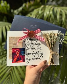 someone holding up a birthday card in front of some plants and trees with the words happy birthday to the one who lights up my world