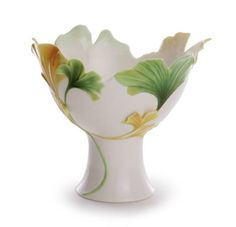 a white vase with yellow and green flowers on it's side, sitting in front of a white background