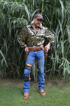 a man standing in front of a bamboo tree wearing jeans and a cowboy hat with his hands on his hips