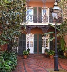 an old fashioned house with green shutters on the front and second story, surrounded by greenery