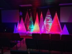 brightly lit christmas trees sit in front of an empty auditorium stage with chairs on the side