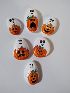 five painted rocks with faces and eyes on them are arranged in the shape of pumpkins