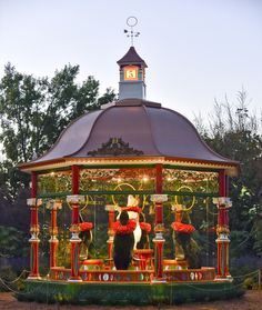 a gazebo with people sitting on it in the middle of some flowers and trees