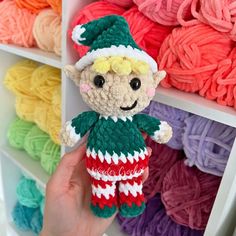 a hand holding a small crocheted elf doll in front of colorful yarns