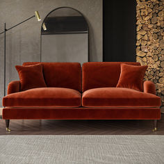 an orange couch sitting in front of a mirror on top of a wooden floor next to a lamp