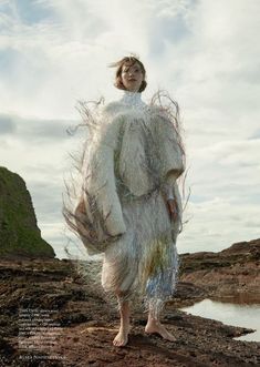 a woman standing on top of a dirt field next to a body of water and grass