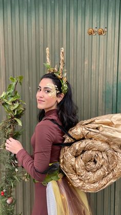 a woman is dressed up as a fairy holding a tree branch and wrapped in gold foil