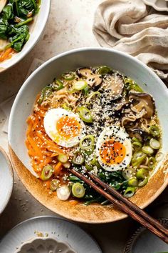 two bowls filled with vegetables and eggs on top of a white tablecloth next to chopsticks