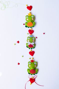 three frog ornaments are hanging on the wall next to confetti hearts and streamers