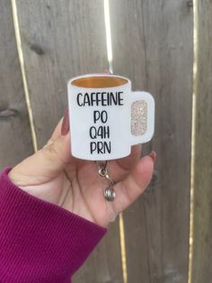 someone holding up a coffee mug keychain that says caffeine do ah prin