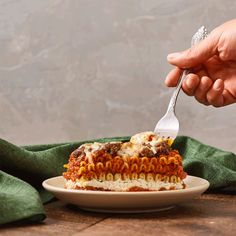 a person is holding a fork over a piece of lasagna on a plate