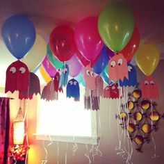 a bunch of balloons are hanging from the ceiling in front of a window with pacman faces on them