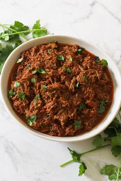 a white bowl filled with shredded meat and garnished with cilantro leaves