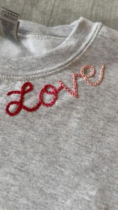 a gray shirt with the word love embroidered on it's chest and red thread