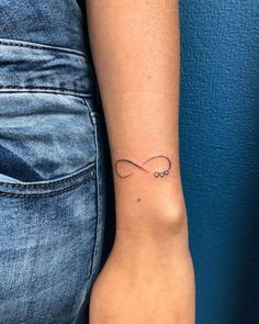 a woman's wrist with an infinite symbol tattoo on her left arm, in front of a blue wall