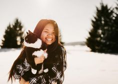 a woman holding a black and white cat in the snow