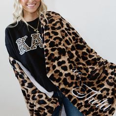 a woman is wearing a leopard print blanket and smiling at the camera while standing in front of a white wall