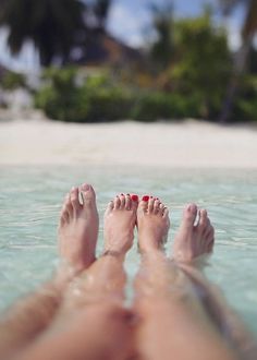 two people laying in the water with their feet up and one person wearing red nail polish