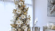 a decorated christmas tree with white flowers and gold ornaments in front of a large window