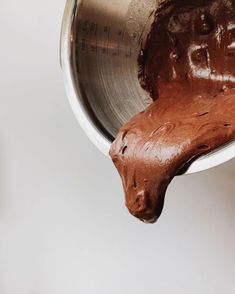 a metal bowl filled with chocolate frosting on top of a white counter next to a measuring cup